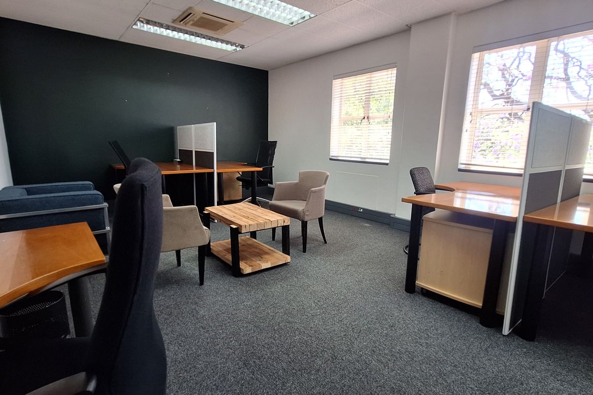 A functional office space featuring carpeted flooring, recessed lighting, and large windows with venetian blinds, providing a professional work environment.