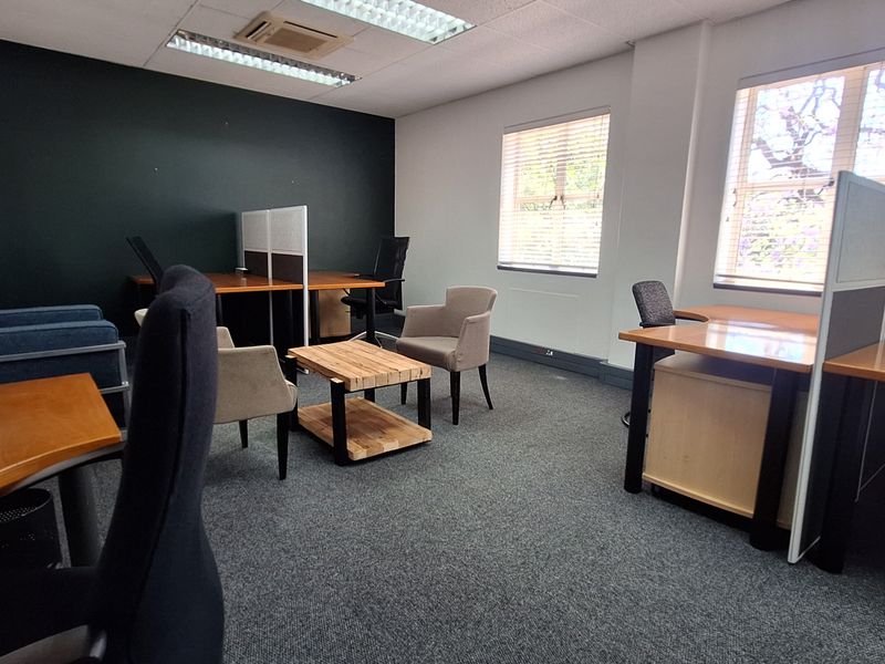 A functional office space featuring carpeted flooring, recessed lighting, and large windows with venetian blinds, providing a professional work environment.