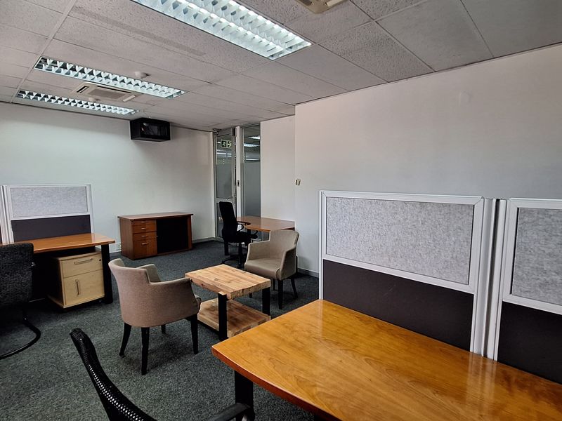 A functional office space featuring carpeted flooring, suspended ceilings with recessed lighting, and a glass partition door.