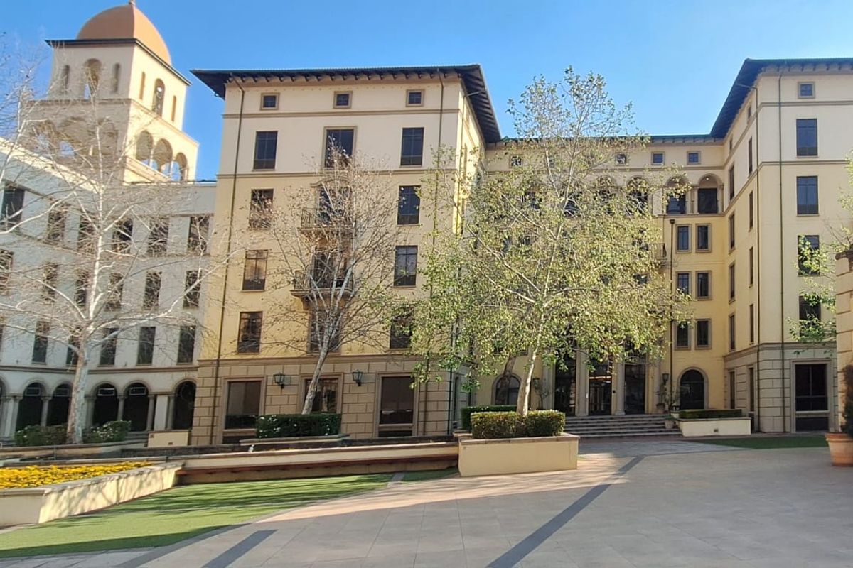 A well-maintained multi-story office building complex featuring a paved courtyard, landscaped planters, and classic architectural elements including arched windows and a prominent tower.