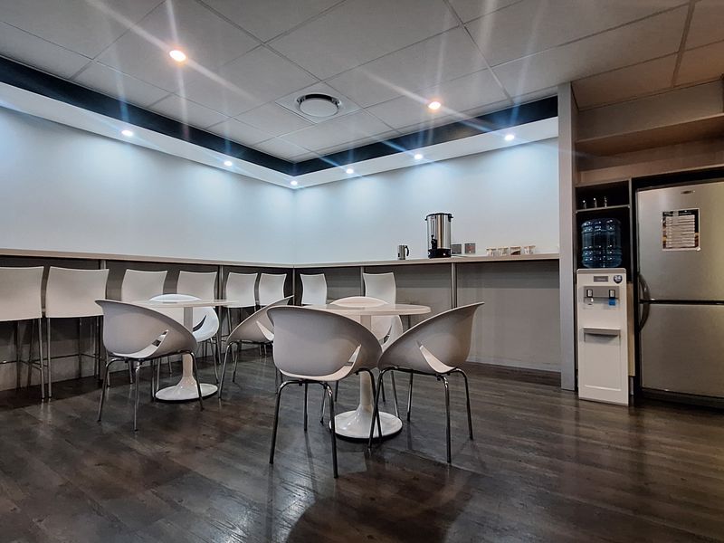 A modern office breakroom featuring laminate flooring, recessed ceiling lighting, and built-in cabinetry with a functional counter space.