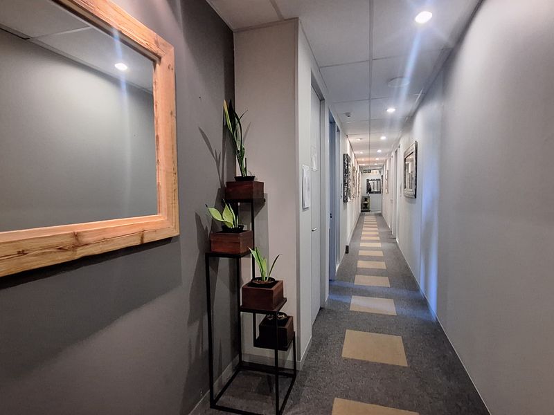 A well-maintained office hallway featuring recessed downlighting, neutral wall finishes, and patterned carpet flooring, providing access to multiple internal office spaces.