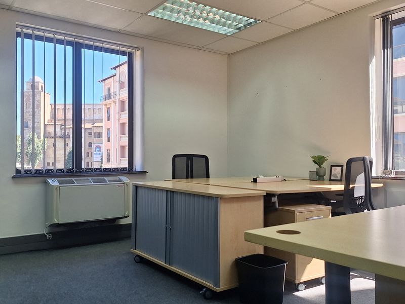 A bright, functional office space featuring large windows with vertical blinds, carpeted flooring, and integrated HVAC climate control.