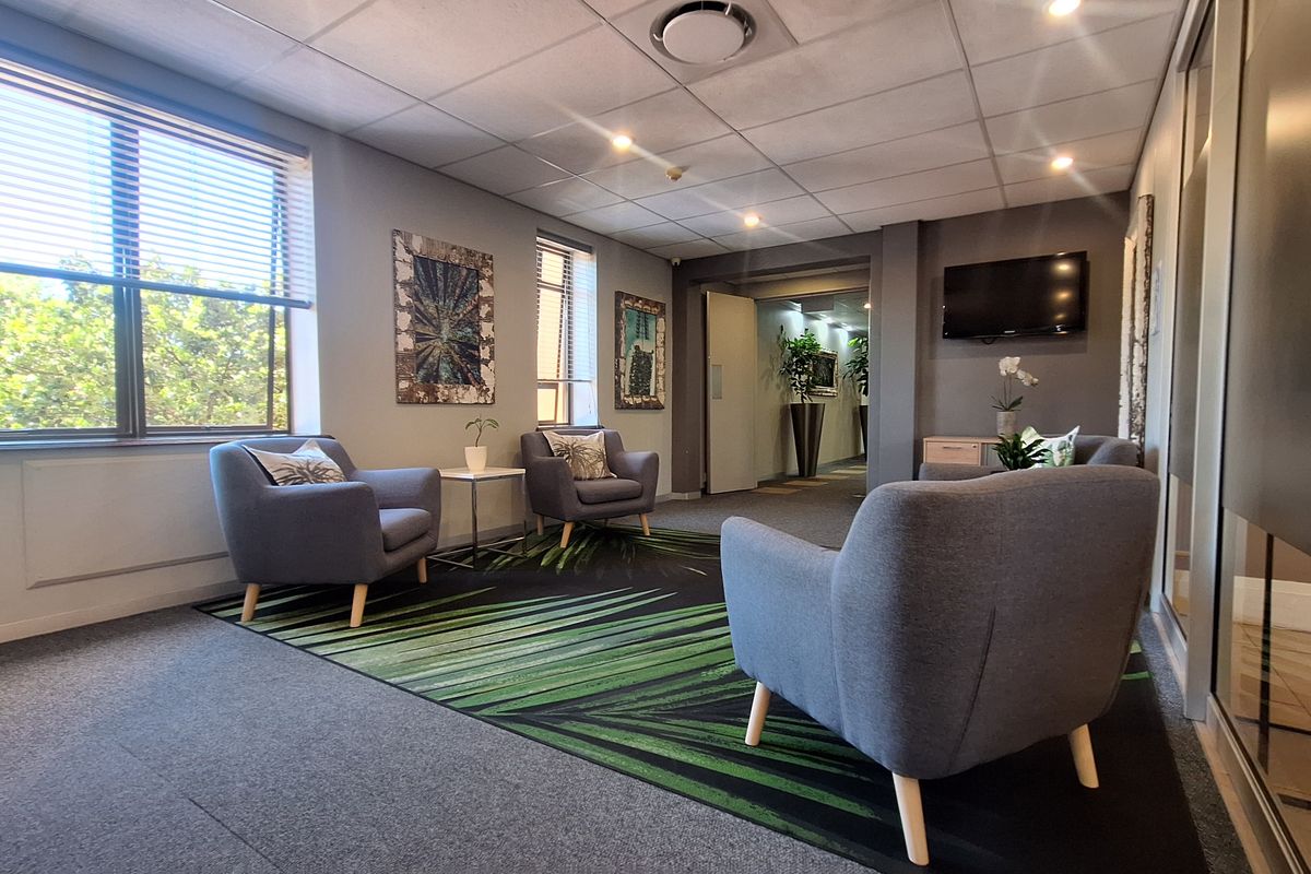 A professional office waiting area featuring carpeted flooring, recessed lighting, and large windows with venetian blinds, creating a bright and welcoming environment.