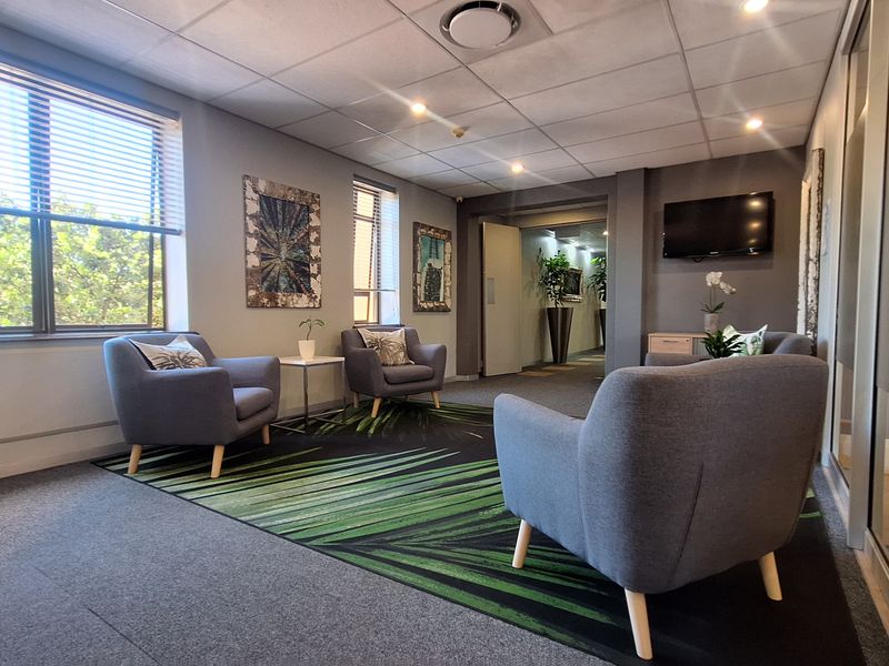 A professional office waiting area featuring carpeted flooring, recessed lighting, and large windows with venetian blinds, creating a bright and welcoming environment.