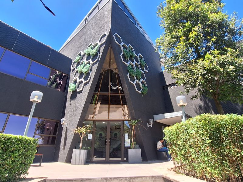 Modern office building entrance featuring a distinctive dark facade with geometric decorative elements, glass doors, and well-maintained surrounding landscaping.
