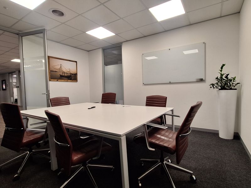 A professional meeting room featuring glass partition walls, a wall-mounted glass whiteboard, recessed lighting, and carpet flooring.