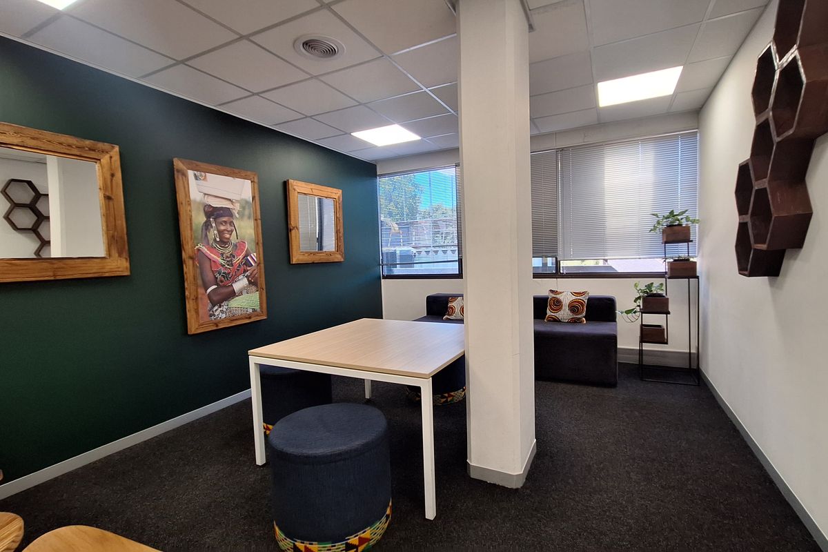A modern office space featuring dark green accent walls, carpeted flooring, a central structural column, and recessed ceiling lighting with large windows and venetian blinds.