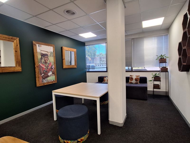 A modern office space featuring dark green accent walls, carpeted flooring, a central structural column, and recessed ceiling lighting with large windows and venetian blinds.