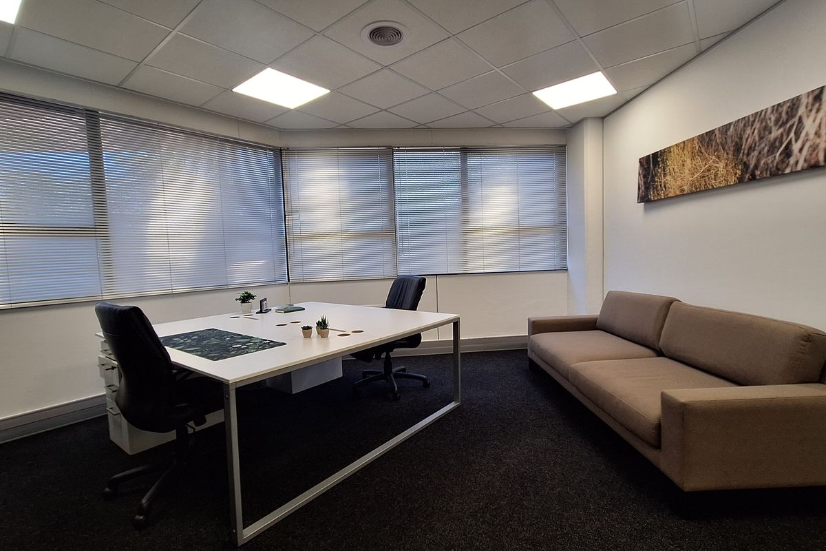A professional office space featuring large windows with venetian blinds, recessed lighting, and dark carpeting, providing a clean and functional work environment.
