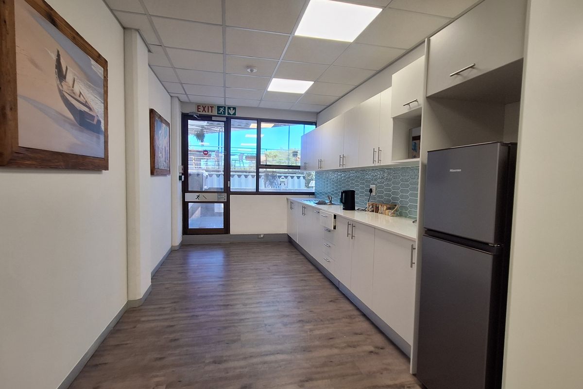 A clean and modern office kitchenette featuring white cabinetry, a tiled backsplash, laminate flooring, and a drop ceiling with recessed lighting.