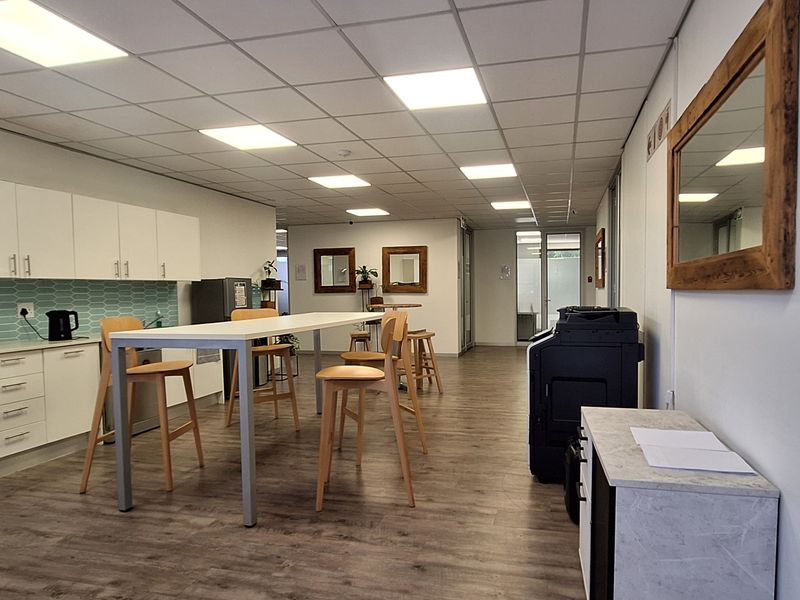 A modern office breakroom featuring built-in cabinetry, a tiled backsplash, recessed ceiling lighting, and durable laminate flooring in a clean, professional workspace environment.
