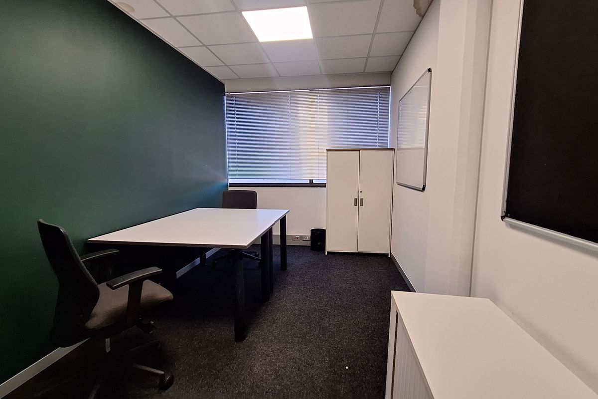 A functional office space featuring dark green accent wall, carpeted flooring, suspended ceiling with recessed lighting, and window blinds.
