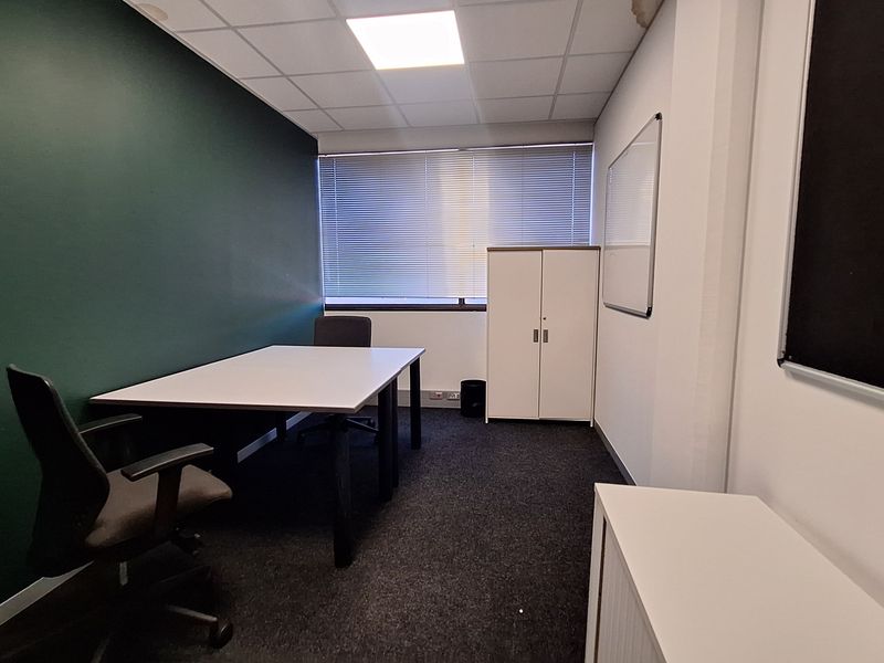 A functional office space featuring dark green accent wall, carpeted flooring, suspended ceiling with recessed lighting, and window blinds.
