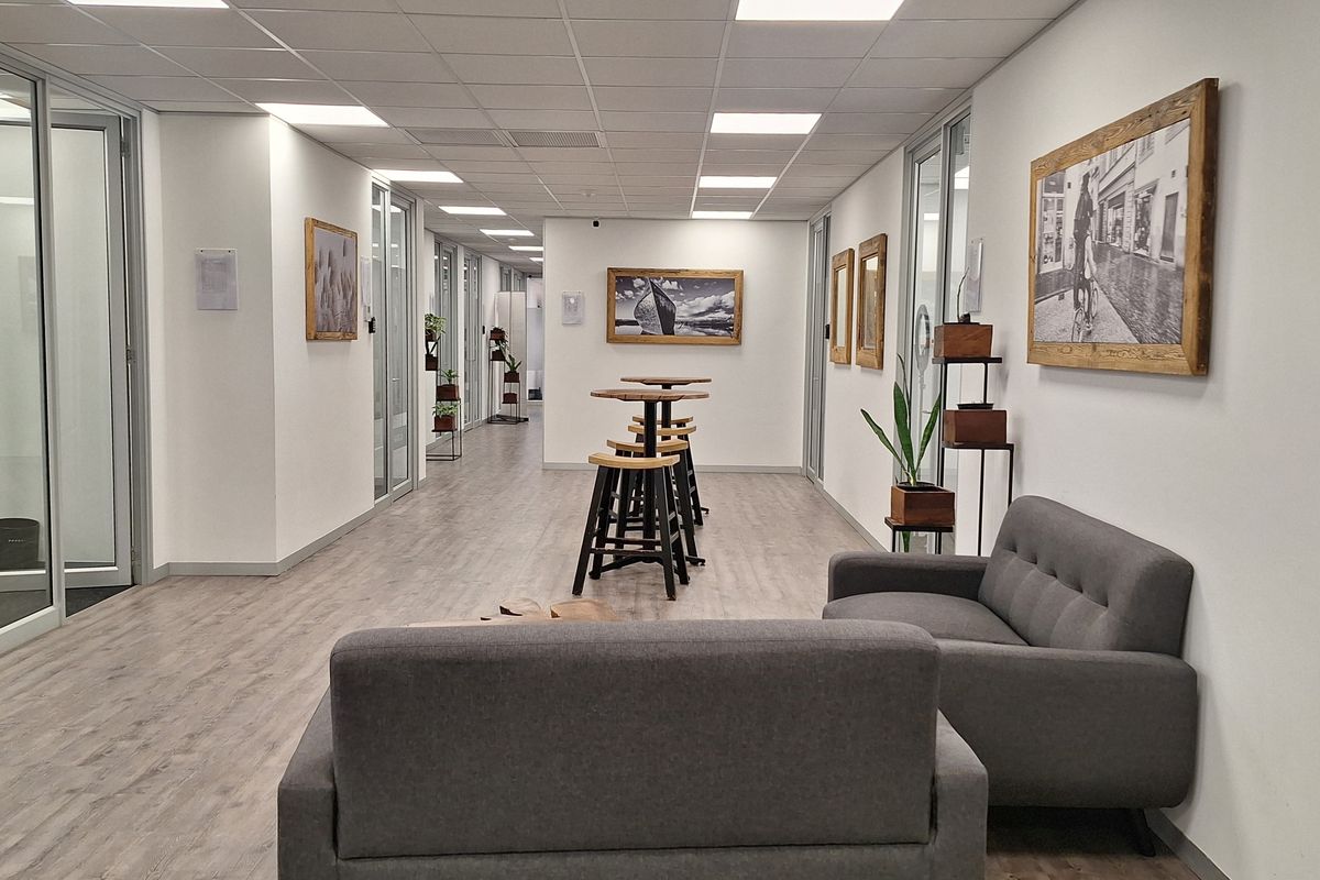 A modern office corridor featuring glass-partitioned rooms, suspended ceiling with recessed lighting, and durable laminate flooring in a professional workspace environment.