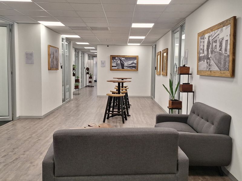 A modern office corridor featuring glass-partitioned rooms, suspended ceiling with recessed lighting, and durable laminate flooring in a professional workspace environment.