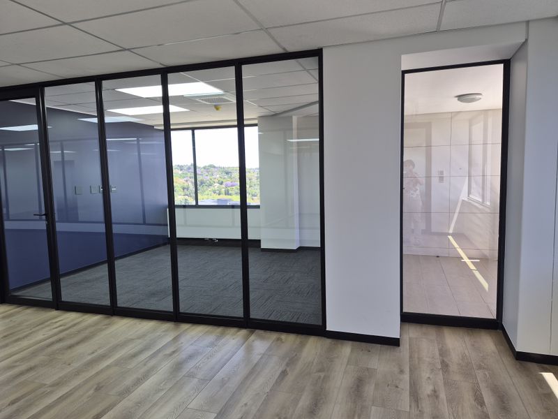 Modern office space featuring glass partition walls, suspended ceilings, and a combination of carpet and laminate flooring with natural light.