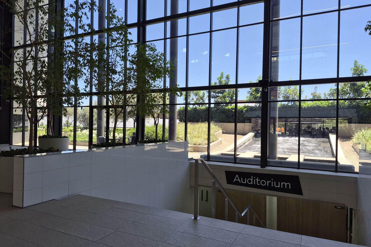 Modern office building entrance featuring a grand floor-to-ceiling glass facade, tiled flooring, and a staircase leading down to the auditorium.