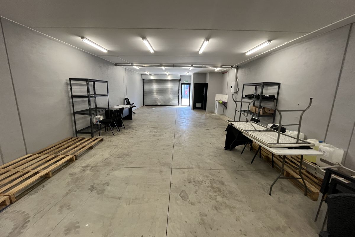 Spacious industrial utility area featuring concrete flooring, roller shutter door access, and overhead fluorescent lighting, suitable for storage or workshop use.