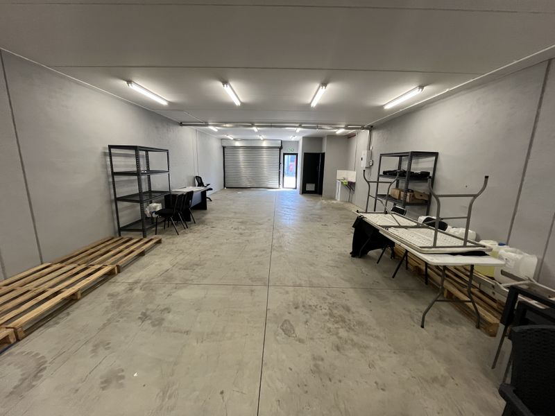Spacious industrial utility area featuring concrete flooring, roller shutter door access, and overhead fluorescent lighting, suitable for storage or workshop use.