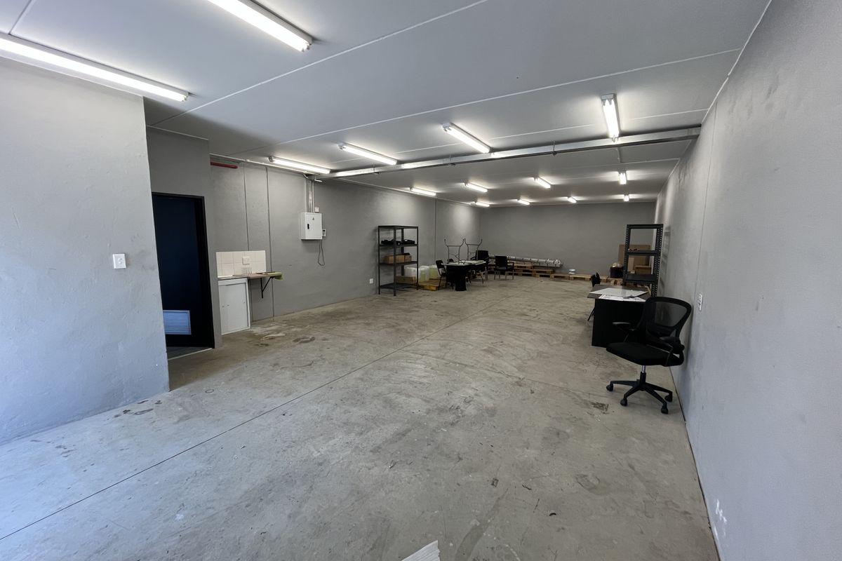 Spacious industrial utility area featuring concrete flooring, fluorescent lighting, and a small kitchenette sink unit, suitable for storage or workshop use.