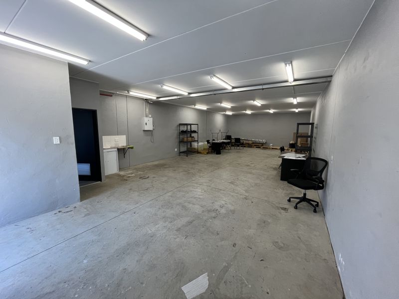 Spacious industrial utility area featuring concrete flooring, fluorescent lighting, and a small kitchenette sink unit, suitable for storage or workshop use.