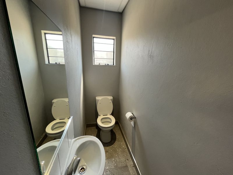 A compact, functional guest bathroom featuring a toilet, wall-mounted basin with mixer tap, and a large wall mirror.