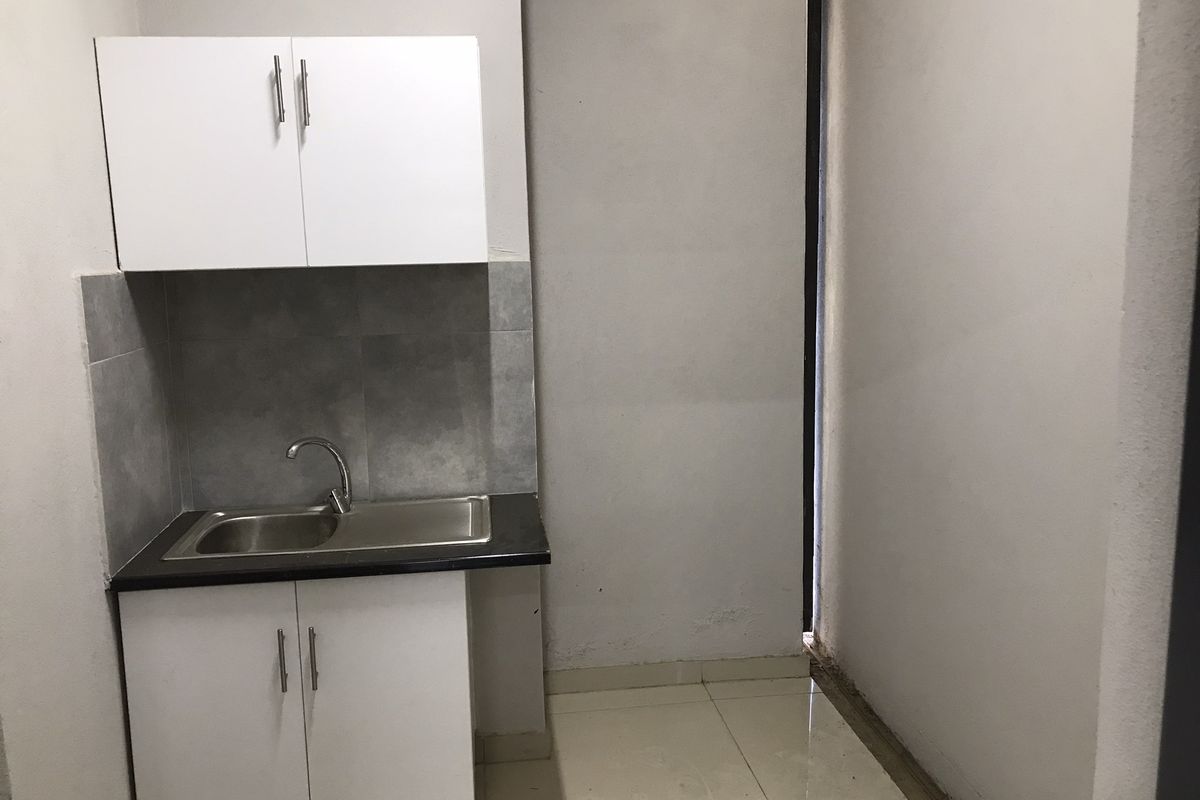 A compact kitchenette featuring white cabinetry, a stainless steel sink, and tiled splashback, suitable for a small office or utility space.