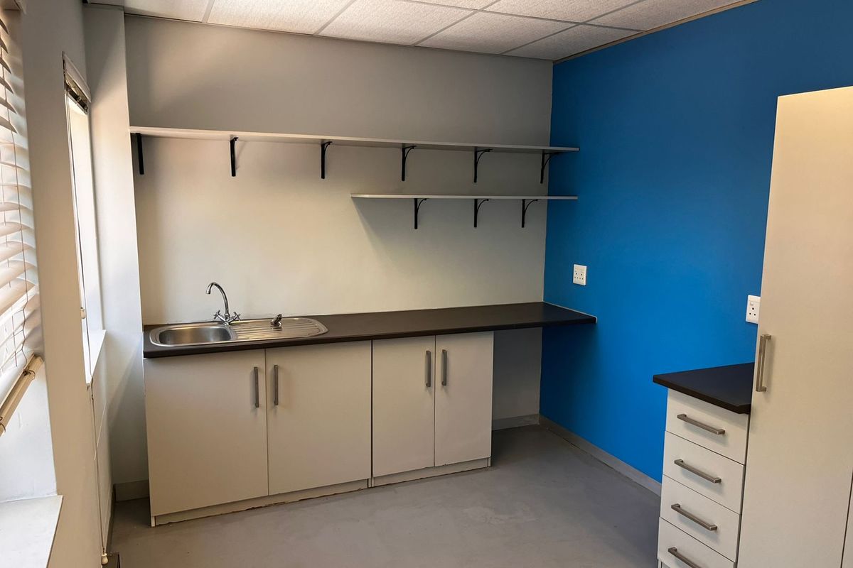 A functional office kitchenette featuring built-in cabinetry, a stainless steel sink, laminate countertops, and open wall shelving.