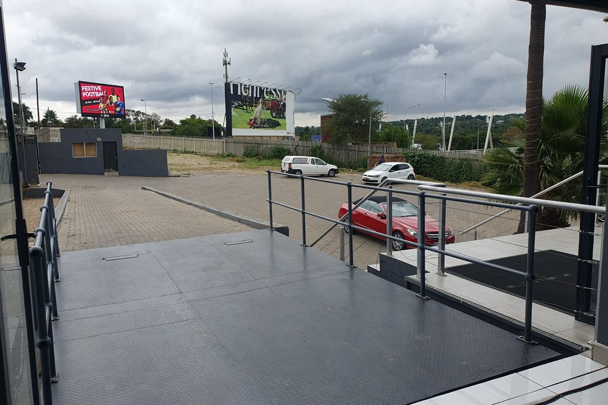 View from a raised metal loading platform overlooking a paved parking area and commercial exterior space.
