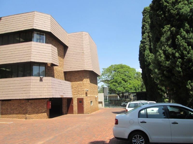 Exterior view of a multi-story office building featuring a brick facade, mansard-style roof, and a paved driveway entrance.