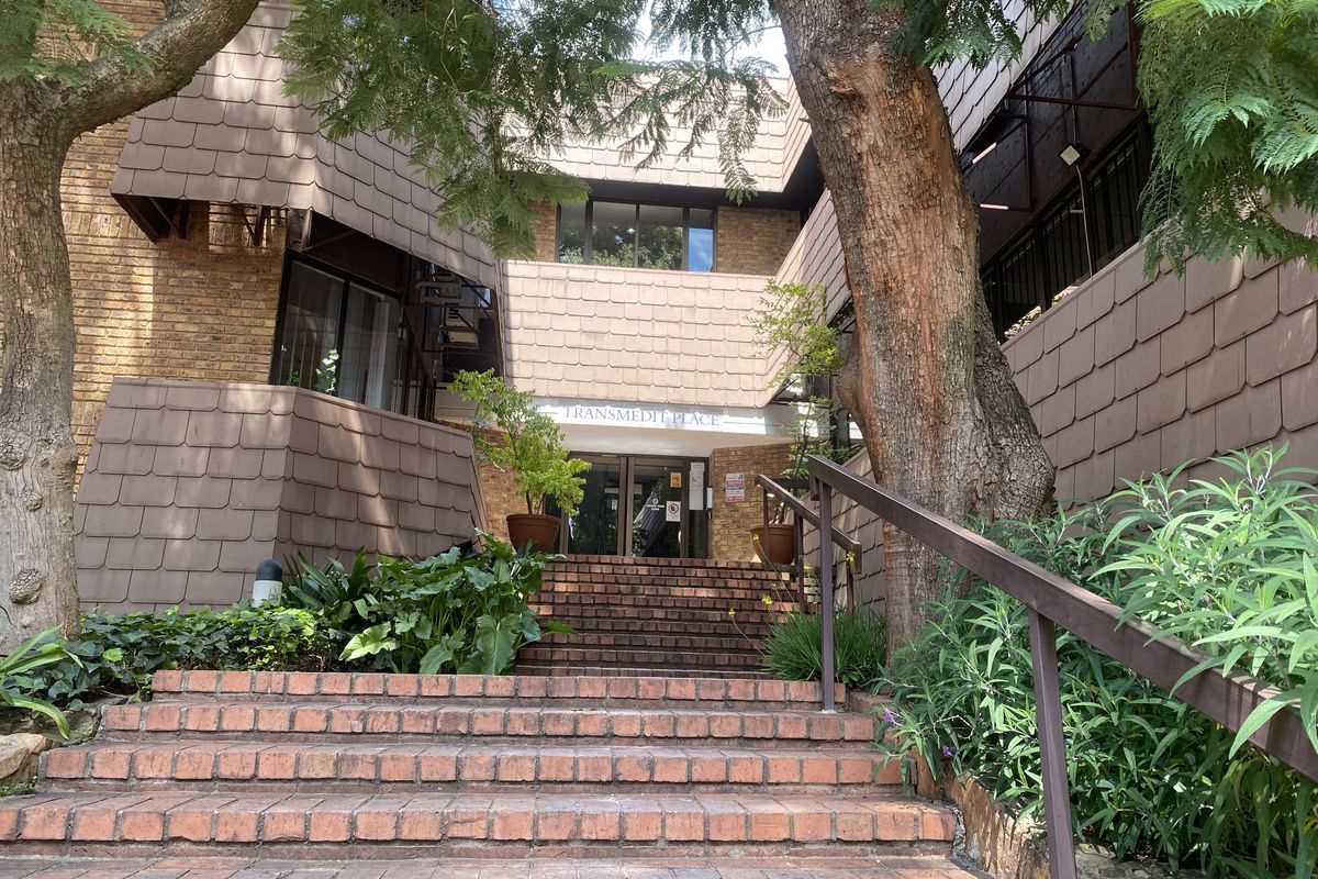 Front entrance of Transmedit Place featuring a brick staircase, metal handrails, and a multi-level brick and tile facade.