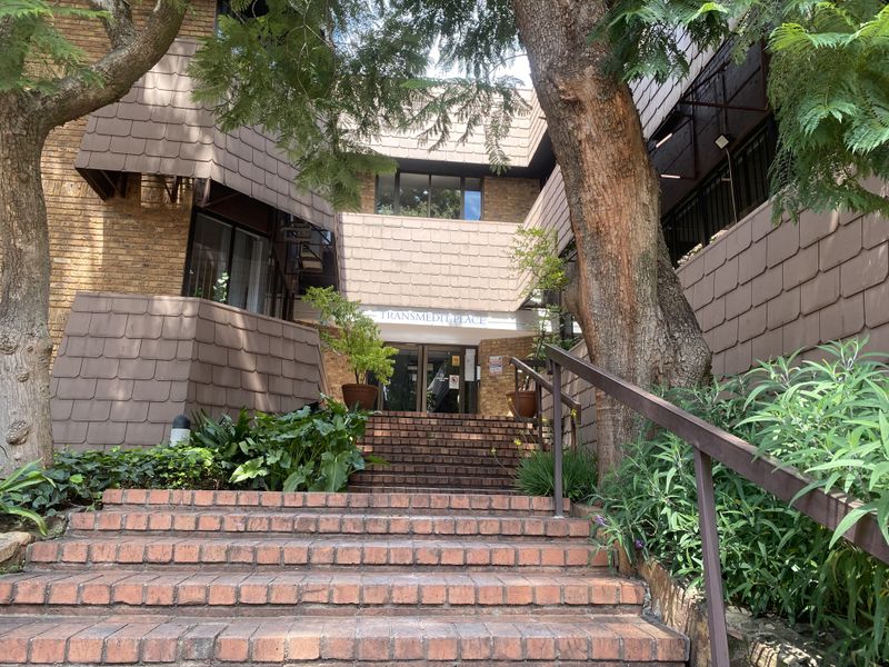 Front entrance of Transmedit Place featuring a brick staircase, metal handrails, and a multi-level brick and tile facade.
