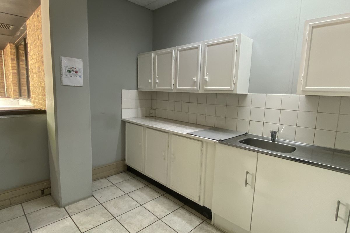 A functional office kitchenette featuring built-in white cabinetry, a stainless steel sink, tiled backsplash, and tiled flooring.