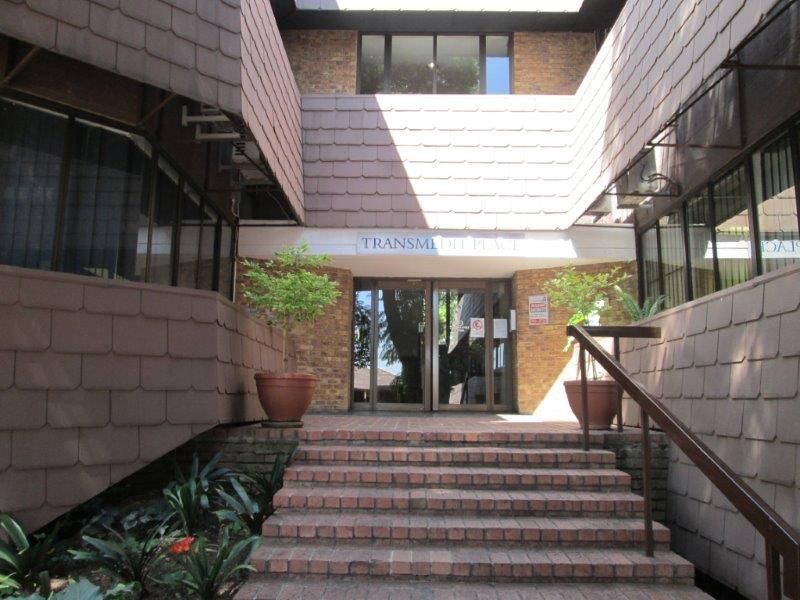 Front entrance of Transmed Place office building featuring a brick staircase, glass doors, and distinctive shingle-style exterior cladding.