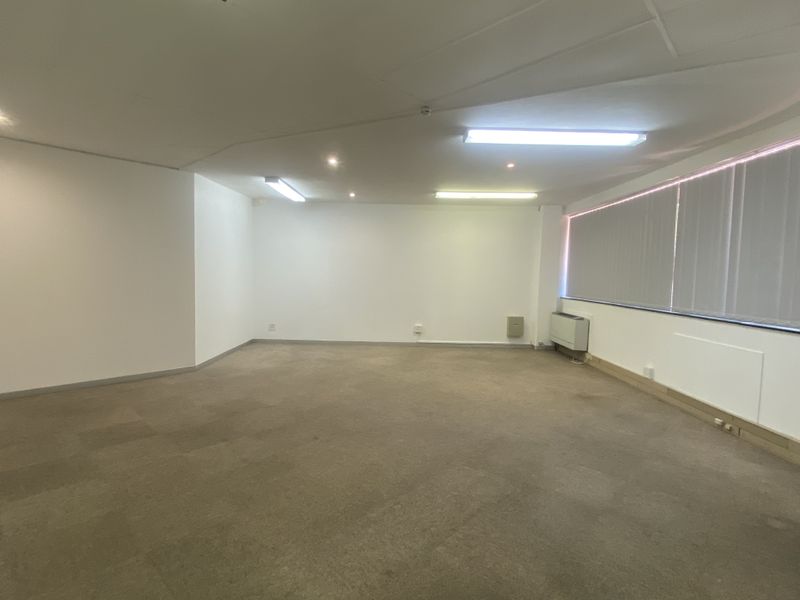 A spacious, empty office area featuring neutral walls, carpeted flooring, and large windows with vertical blinds, providing a blank canvas for professional use.