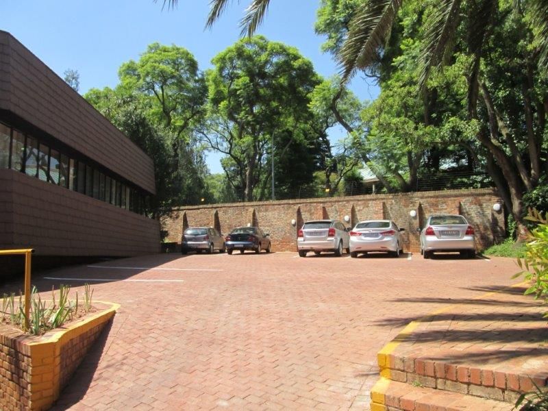 A paved outdoor parking area featuring a brick retaining wall, mature trees, and exterior wall lighting, providing functional space for the office property.