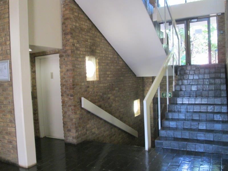 Office building entrance foyer featuring exposed brick walls, a tiled staircase with metal handrails, and natural light from the glass entrance door.