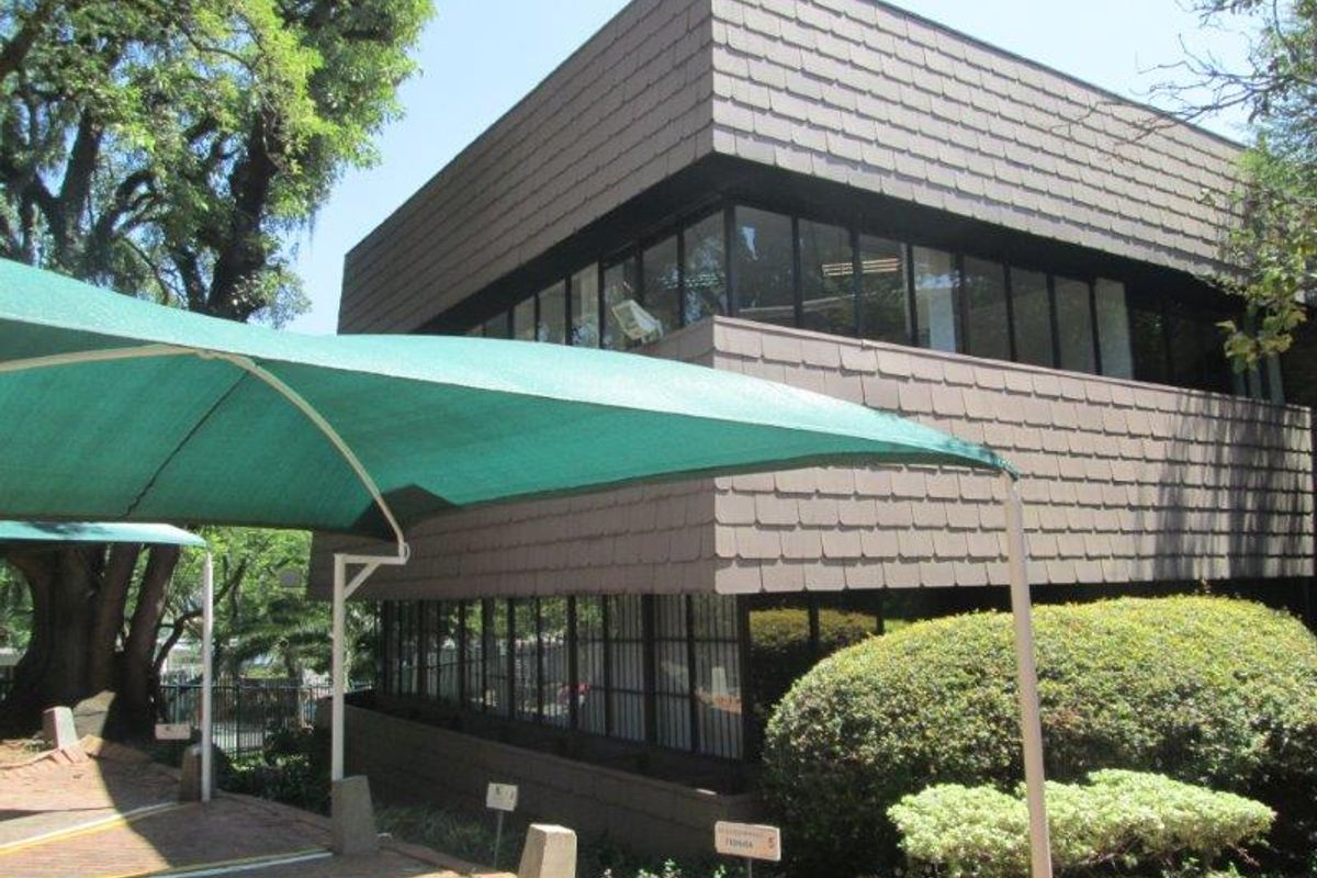 Exterior view of a two-story office building featuring a shingle facade, large windows, and a covered parking area with a shade sail.