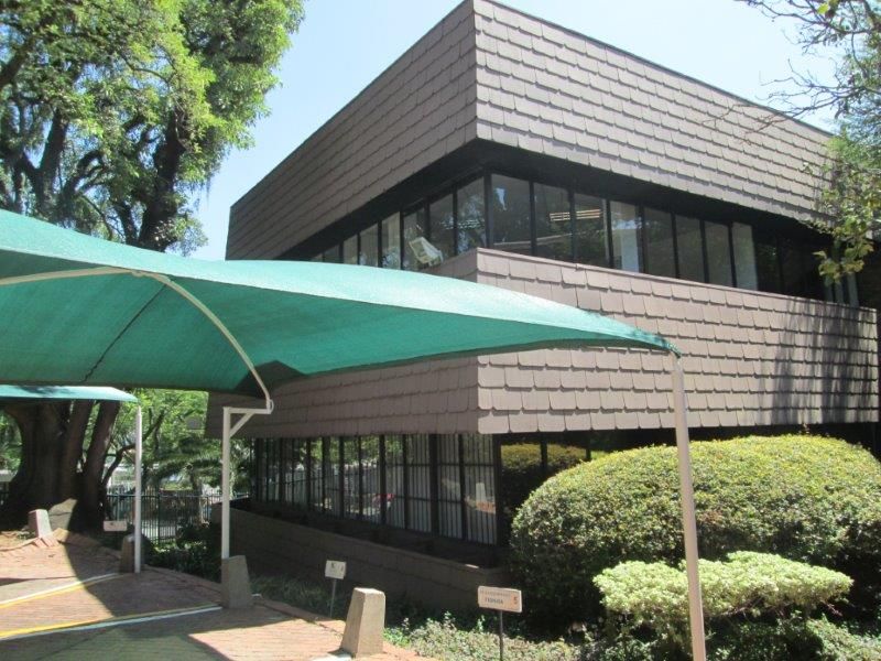 Exterior view of a two-story office building featuring a shingle facade, large windows, and a covered parking area with a shade sail.