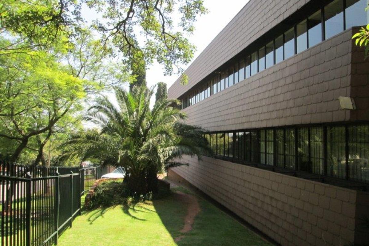Exterior view of the office building featuring a tiled facade, continuous ribbon windows, and a well-maintained garden area with security fencing.