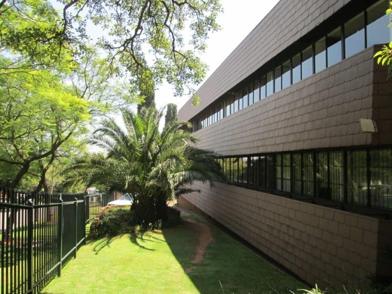 Exterior view of the office building featuring a tiled facade, continuous ribbon windows, and a well-maintained garden area with security fencing.