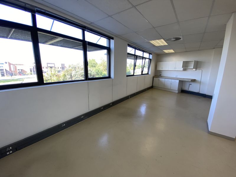 A bright, open-plan office space featuring large windows, a built-in kitchenette, suspended ceilings, and perimeter trunking for convenient workstation connectivity.