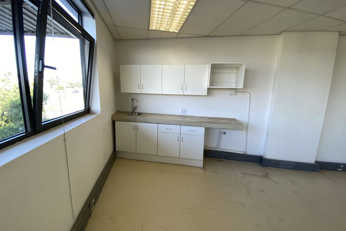 A small office kitchenette featuring built-in white cabinetry, a sink, and a drop ceiling, currently in need of cosmetic updates.