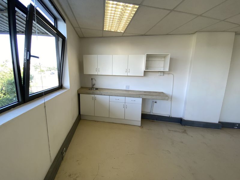 A small office kitchenette featuring built-in white cabinetry, a sink, and a drop ceiling, currently in need of cosmetic updates.