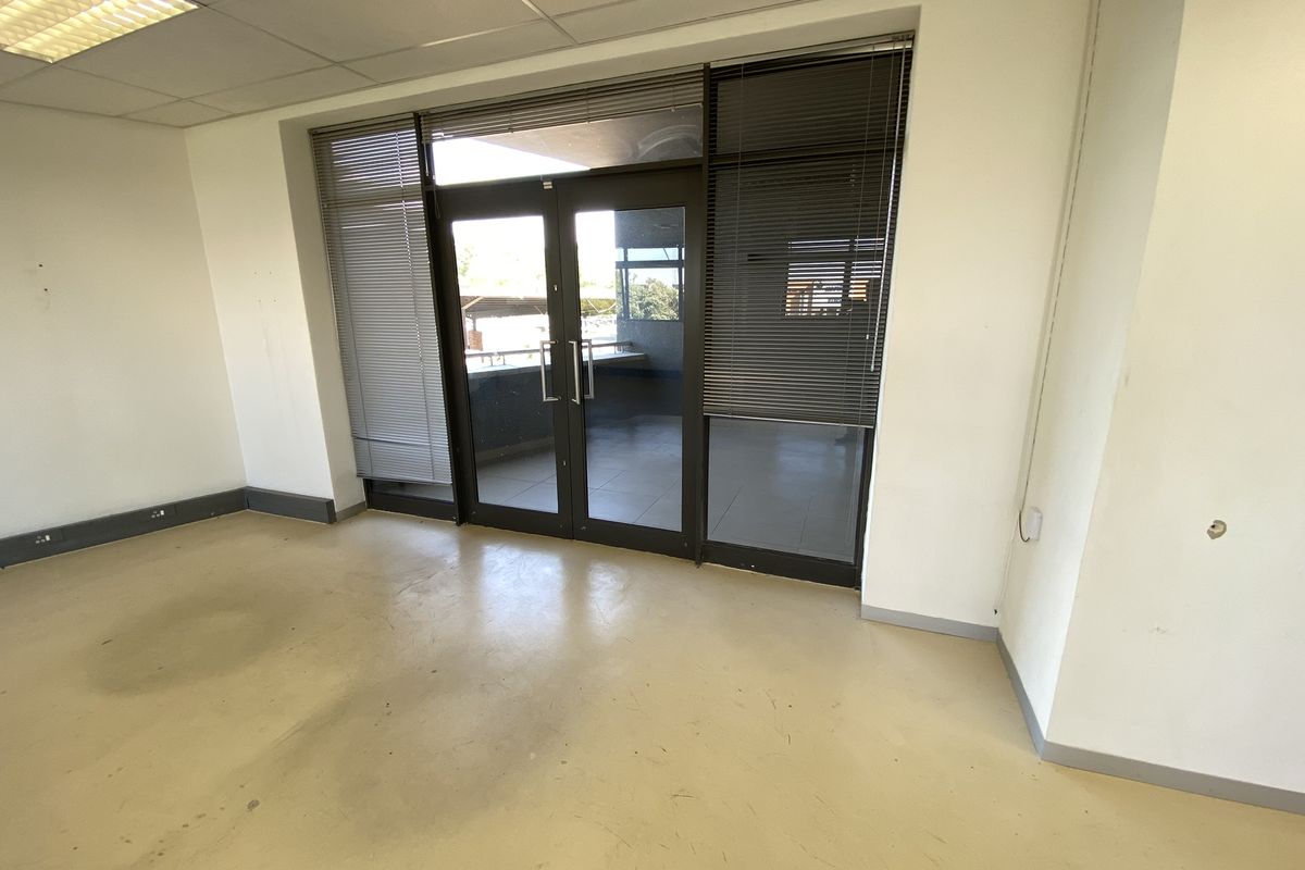 An empty office space featuring vinyl flooring, suspended ceilings with recessed lighting, and double glass doors leading to an exterior balcony area.