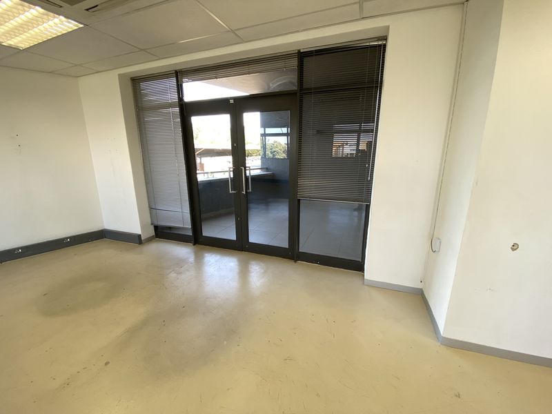 An empty office space featuring vinyl flooring, suspended ceilings with recessed lighting, and double glass doors leading to an exterior balcony area.