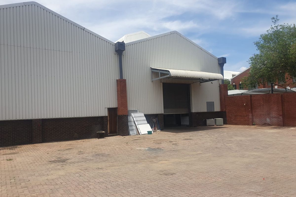 Industrial warehouse exterior featuring corrugated metal cladding, brick base, roller shutter door, and a paved yard area.