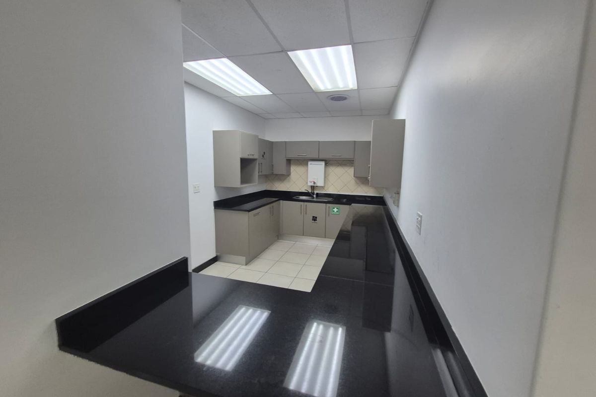 A functional office kitchenette featuring built-in cabinetry, dark granite countertops, a stainless steel sink, and recessed ceiling lighting.