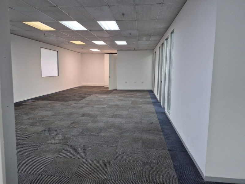 An empty, open-plan office space featuring suspended ceilings, recessed lighting, and carpet tile flooring, offering a versatile layout for various business configurations.